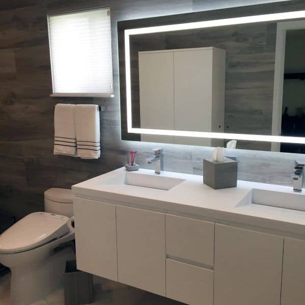 White modern bathroom vanity with a backlit mirror, dual sinks, and sleek cabinetry.
