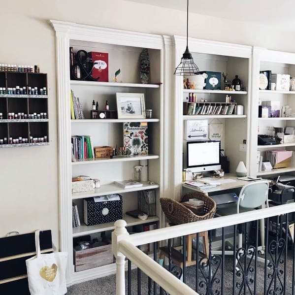 Functional home office with built-in bookcases featuring open shelving and integrated desk spaces. The design is complemented by clean white trim and a rustic hanging pendant light, creating a cozy and productive workspace.