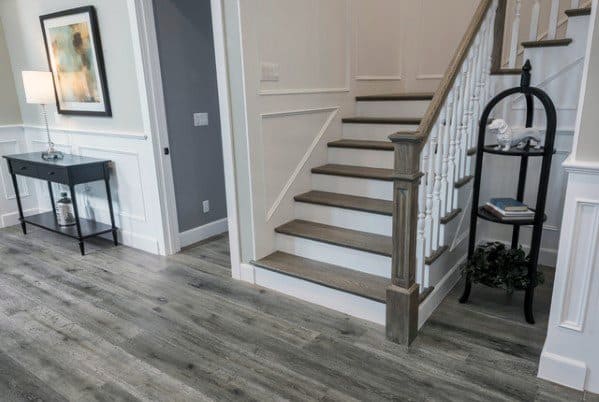 White staircase with vertical railing and wooden steps in a modern entryway with grey flooring.