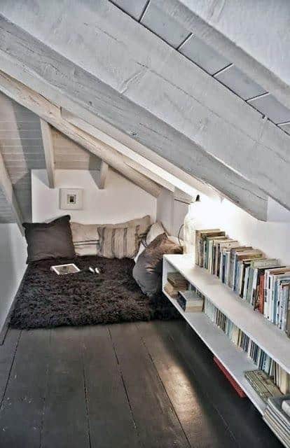 Cozy attic reading nook with plush cushions, a dark shag rug, and white shelves filled with books