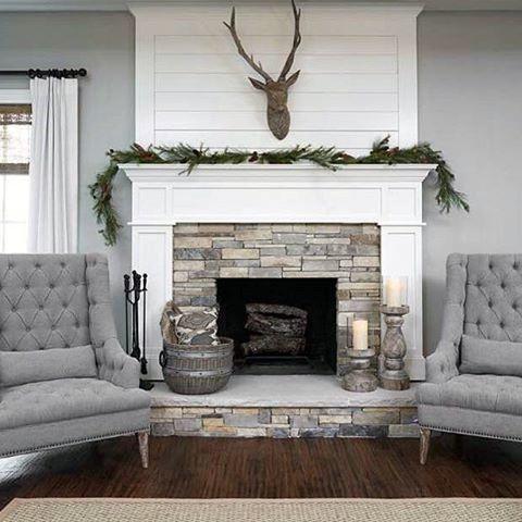 White shiplap fireplace with stone surround, decorated mantel, and tufted gray armchairs.