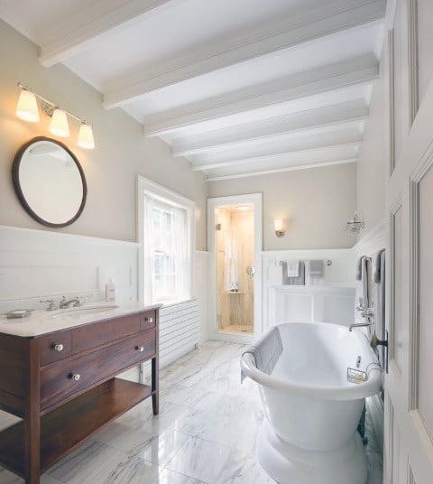 Bright bathroom with white exposed wood beams, freestanding tub, and wooden vanity.