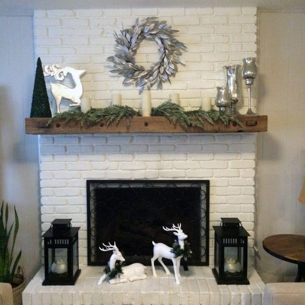 White brick fireplace with Christmas decor, reindeer, lanterns, and a wreath on the mantel.