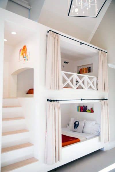 Modern bunk beds with curtains built into white walls, featuring stairs and a small balcony area for extra bunk fun