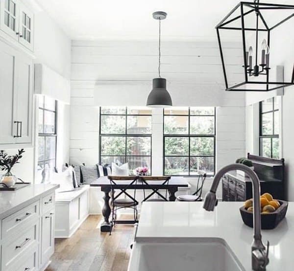 Bright farmhouse kitchen with white cabinets, shiplap walls, black windows, and a cozy dining nook.