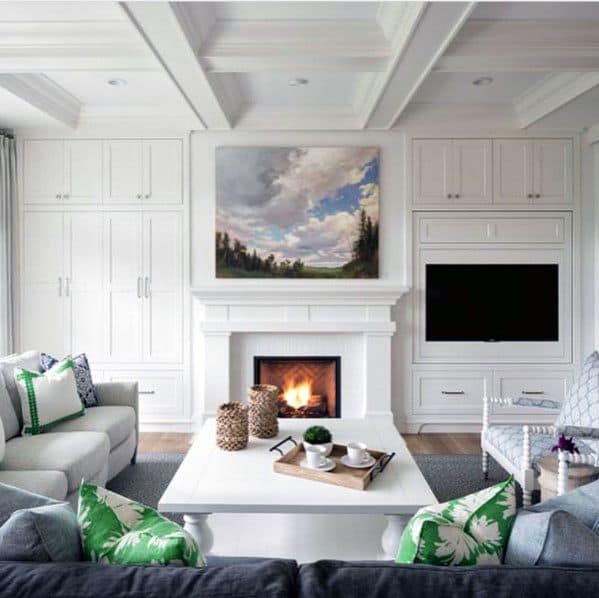 Cozy living room with a fireplace, large TV, white cabinets, and green-accented pillows on gray seating