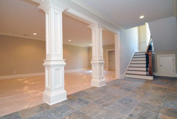 Basement with white decorative columns, tile flooring, and staircase entry.