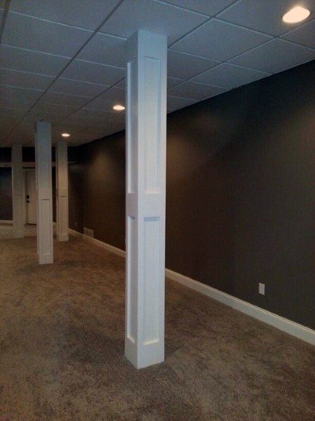 Basement with dark walls, carpet flooring, and white trim-accented support poles.