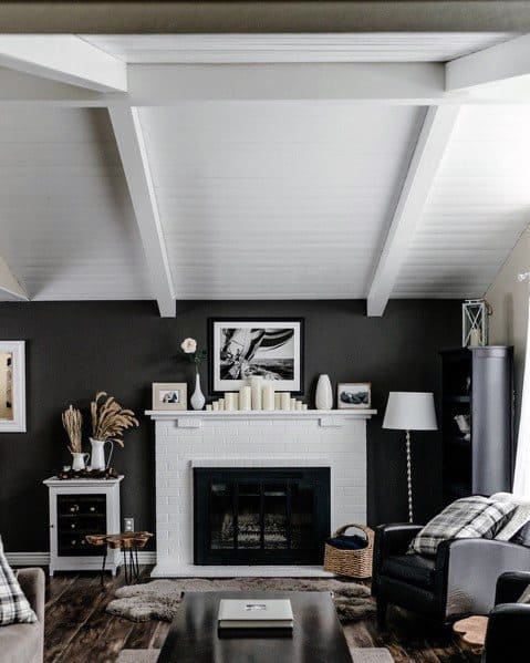 Modern living room with white wood ceiling beams, black walls, and a white brick fireplace.