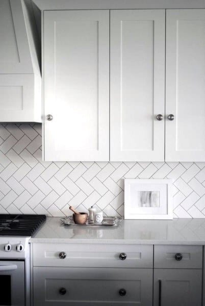 White kitchen with chevron tile backsplash, shaker cabinets, and marble countertop.