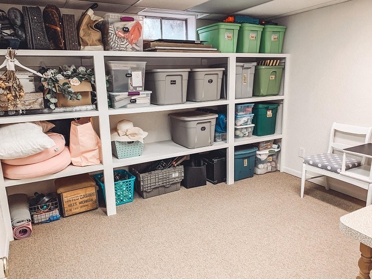 White shelf storage unit in a basement with various bins and containers for organized storage.