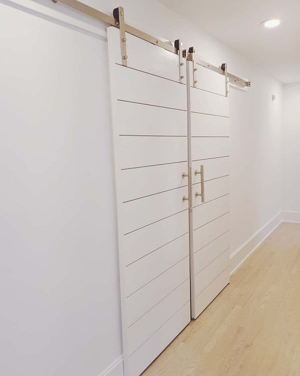 White double sliding barn doors with horizontal grooves and stainless steel handles.