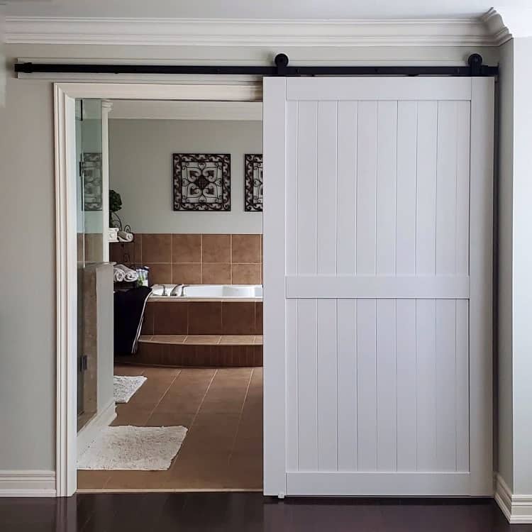 White sliding barn door leading to a bathroom with brown tiles and modern decor.