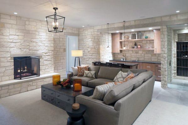 Luxury basement with white stone walls, fireplace, gray sectional couch, and modern wet bar.