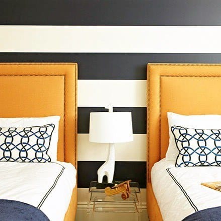 Bedroom with bold navy and white striped walls, paired with vibrant orange headboards.