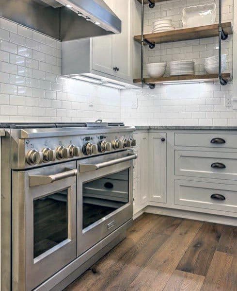 White kitchen with subway tile backsplash, stainless steel oven, and open wooden shelves.