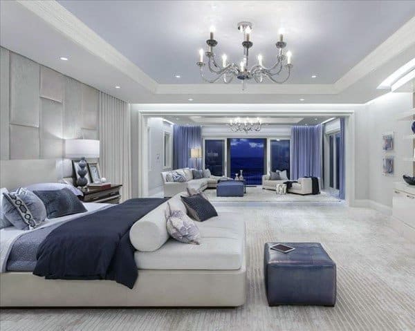 Spacious bedroom with elegant chandeliers, soft blue accents, and a seating area.