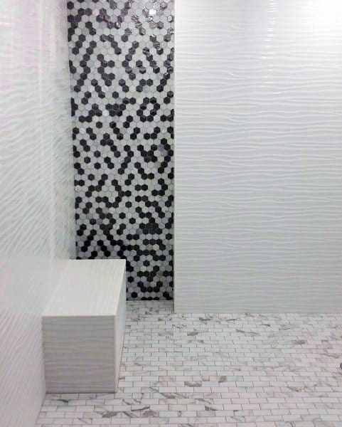 Modern shower with textured white tiles, black and white hexagon accent wall, and bench seating.