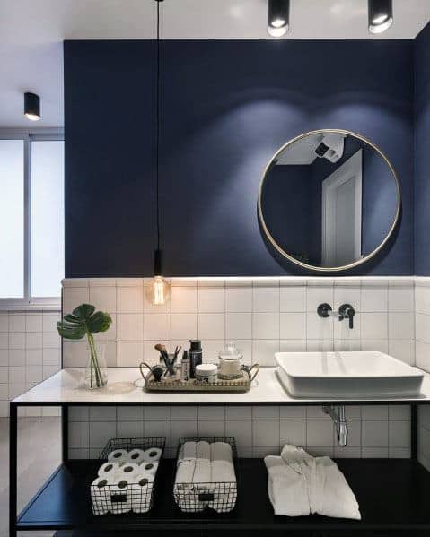 Modern bathroom with navy blue walls, white tiles, a round mirror, and open shelving.