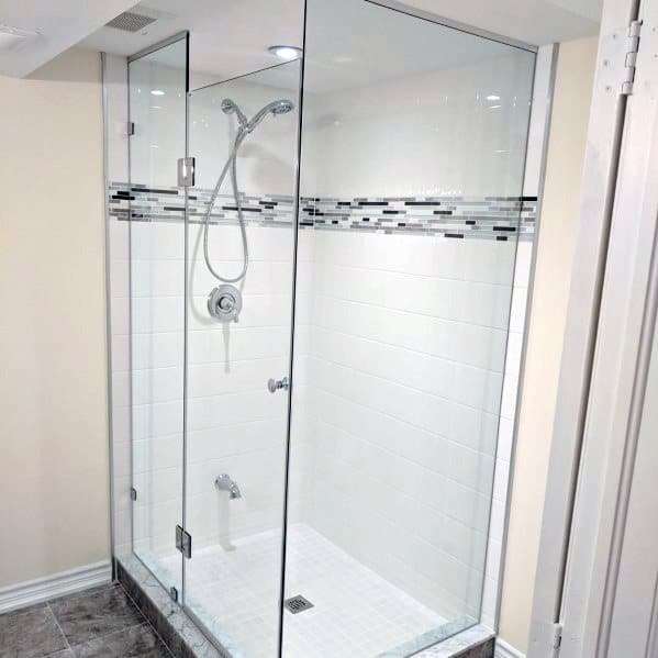 Corner glass shower enclosure with tiled walls and a modern showerhead, next to a tiled bathroom floor