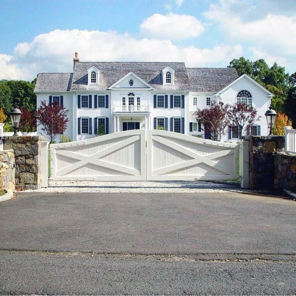 White double driveway gate with cross-brace design, complementing a traditional home facade.