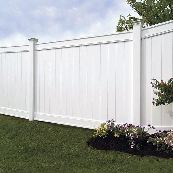 White fence with flowers at the base on a grassy lawn under a cloudy sky