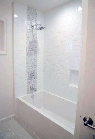 White bathtub with vertical mosaic accent strip and white subway tile walls in bright bathroom.