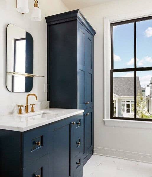 Bathroom with navy blue vanity, tall cabinet, and gold fixtures.