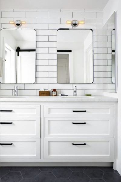 White bathroom vanity with black handles, subway tile backsplash, and dual mirrors.