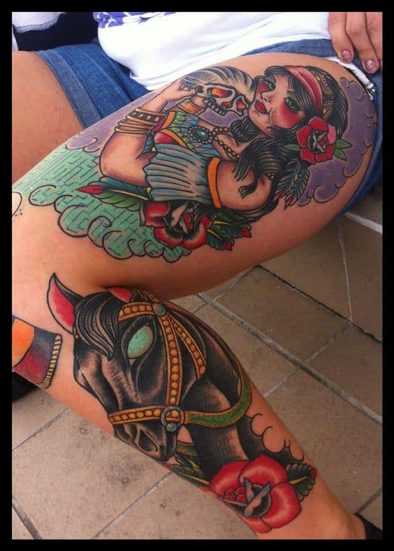 Bold and colorful thigh tattoo of a gypsy woman holding a skull, paired with a detailed black horse head and red roses on the lower leg.