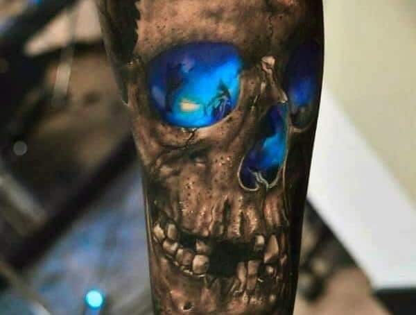 A skull tattoo with vibrant blue eye sockets on a person's forearm