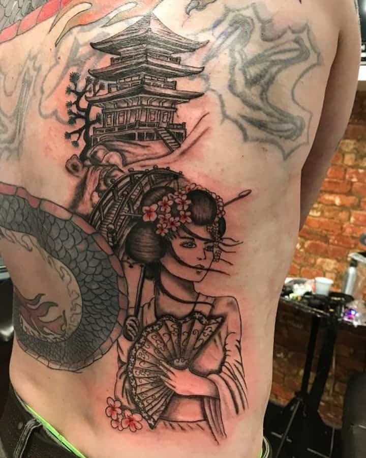 Japanese-style rib tattoo of a Geisha holding a fan, with an intricate pagoda, cherry blossoms, and a partially inked snake wrapping around.