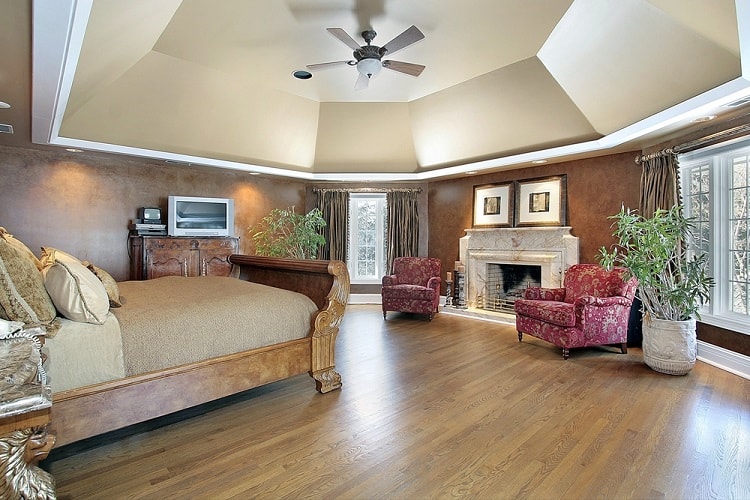 Luxurious bedroom with a grand vaulted ceiling, wooden floor, large bed, fireplace, and elegant armchairs