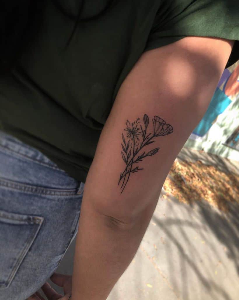 This tattoo features a beautiful design of delicate flowers, including dandelions and other plants, forming a simple, natural motif. The art is well-executed with fine linework, showcasing elegance and nature's beauty.