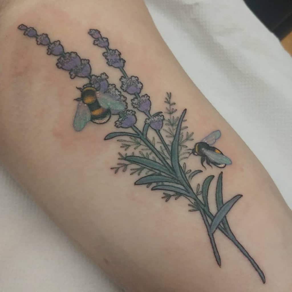 A tattoo featuring two bumblebees hovering over lavender flowers, with detailed greenery and delicate shading.