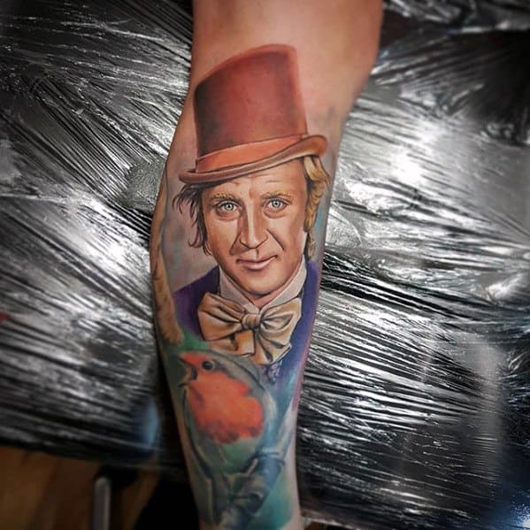 Lifelike Willy Wonka tattoo with a red top hat, soft expression, and a colorful bird perched below, blending fantasy with nature.