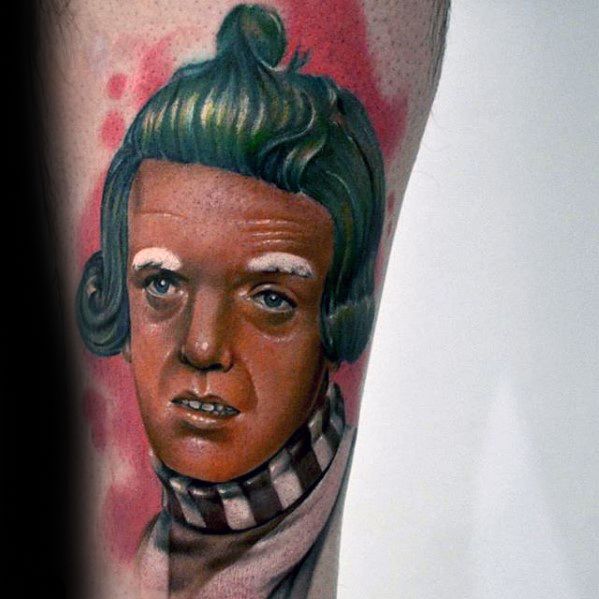Detailed Oompa Loompa tattoo featuring vibrant green hair, white eyebrows, and a brown-and-white collar set against a soft red background.