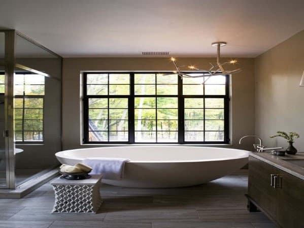 Modern bathroom with a freestanding tub, large window, and decorative side table