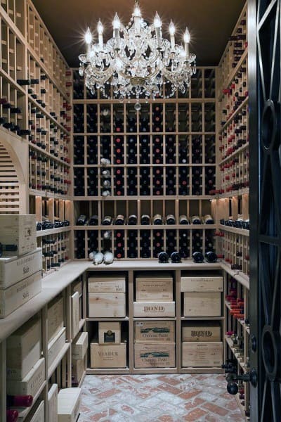 A luxurious wine cellar with wooden racks, wine bottles, a chandelier, and labeled wine boxes on the floor