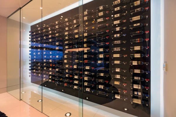 Modern wine cellar with glass walls, showcasing rows of wine bottles on dark shelves, illuminated by soft lighting
