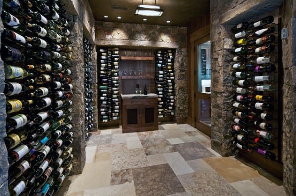 A wine cellar with stone walls, wooden racks brimming with bottles, and a small table in the center