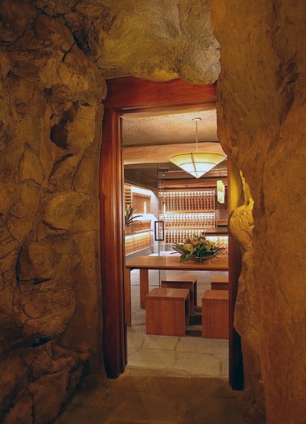 Cozy wine cellar built into a stone cave, with modern wood shelves, a pendant light, and minimalist furniture