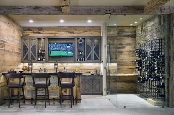Cozy home bar with rustic wood, a TV, two bar stools, and a wine glass-enclosed rack display