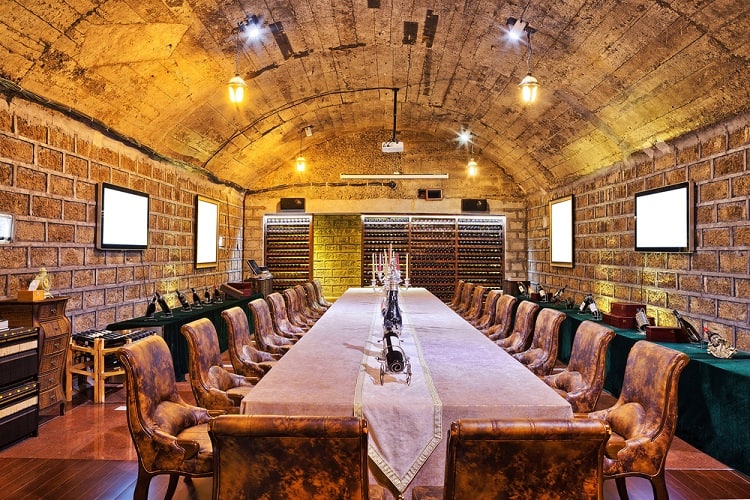 A long, elegant conference table sits beneath an arched stone ceiling with leather chairs and warm lighting