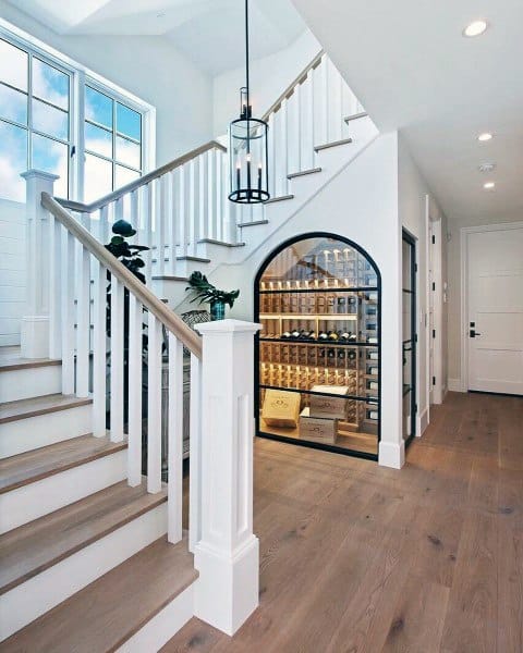 Elegant staircase with white railings and a glass wine cellar beneath, featuring wooden shelves and neatly stored bottles