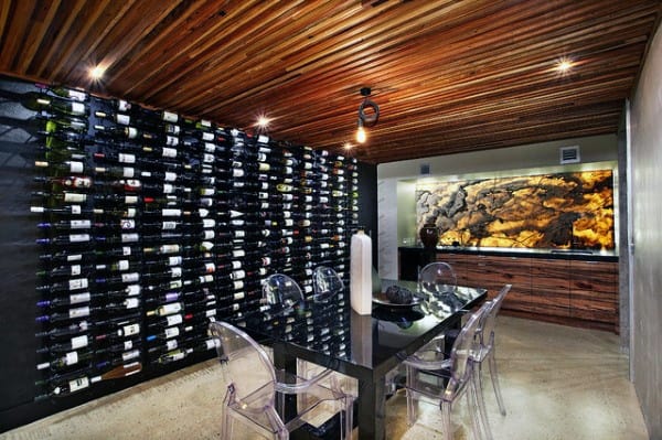 Modern wine cellar with a wall of wine bottles, glass table, transparent chairs, and artistic lighting and decor