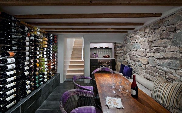 A cozy wine cellar with stone walls, a wooden table set for tasting, and shelves brimming with fine wines