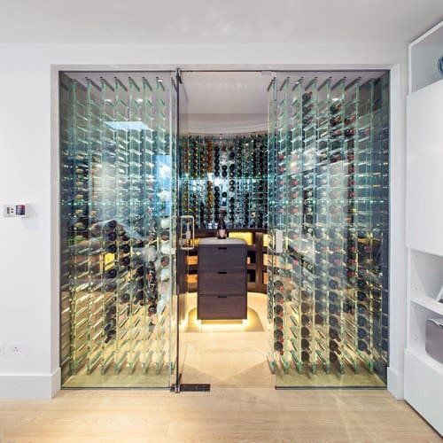 Modern glass-enclosed wine cellar with wall-mounted wine bottles and warm lighting