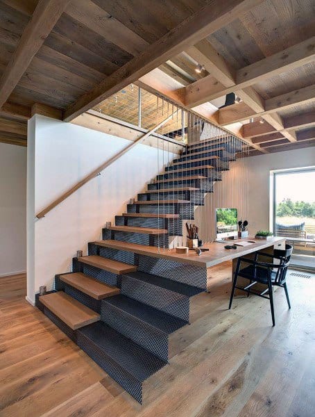 Modern interior with wooden staircase, metal railing, a workspace beneath, large windows, and natural light