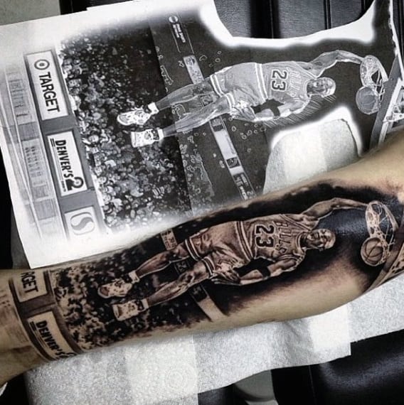 Tattoo of a basketball player dunking a ball on a forearm with a printed image used as reference